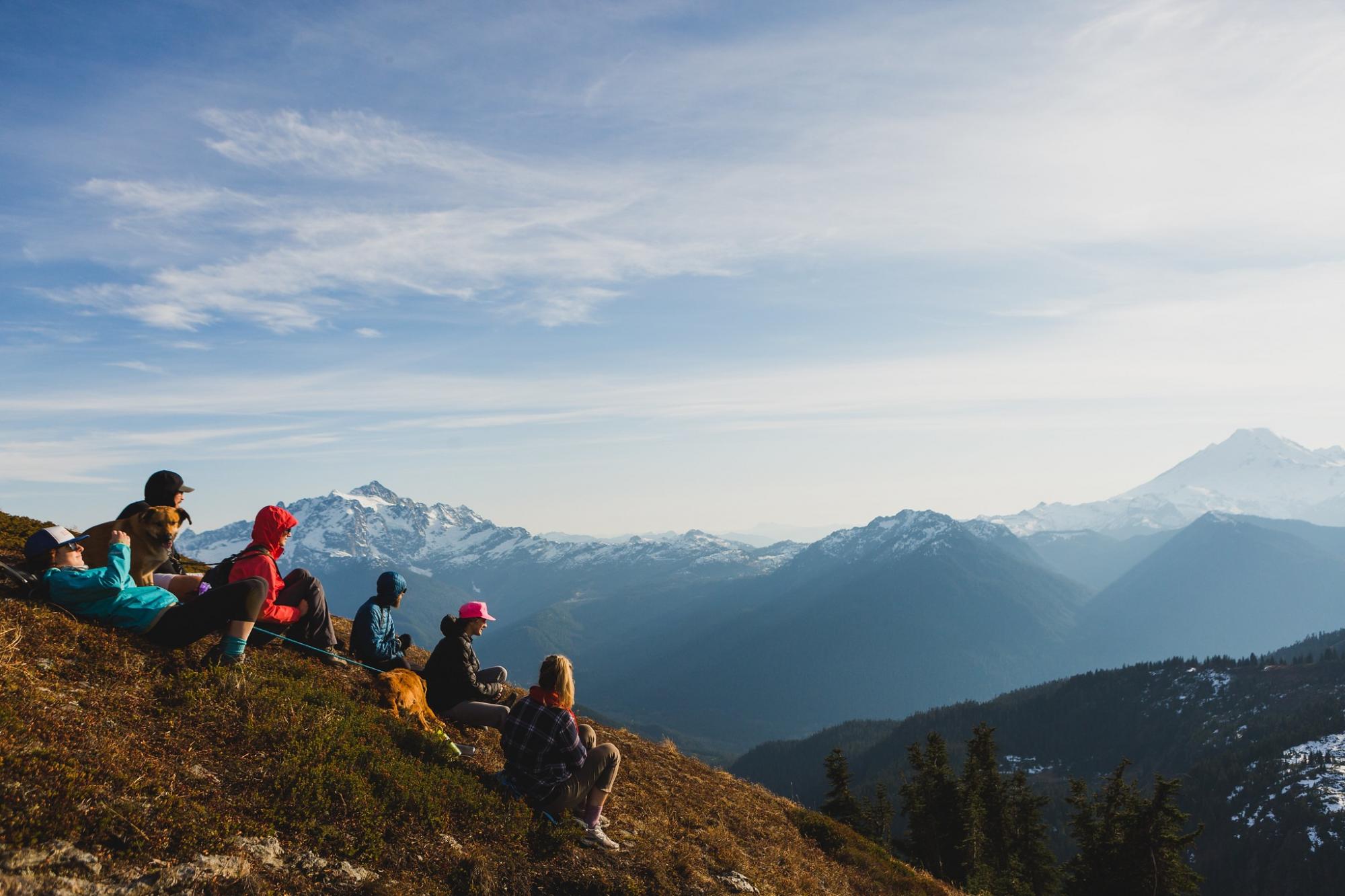 Students sitting on the summit of a mountain looking over a valley to the next mountain range